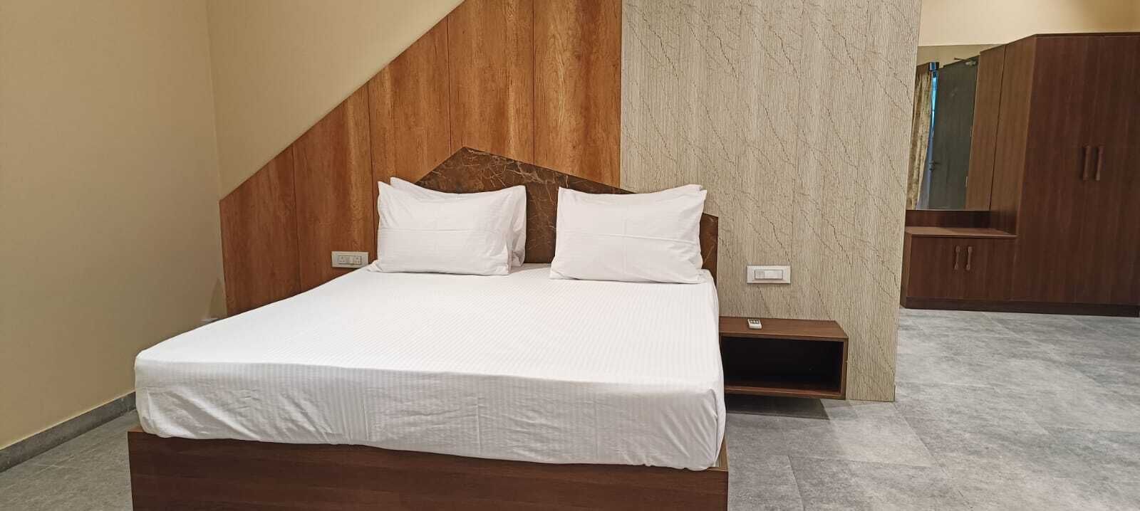 A modern bedroom with a wooden headboard, a large bed with white bedding, a nightstand, and a wardrobe.
