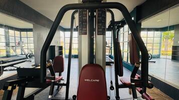 A gym with a red WELLCARE bench, weight machines, and large windows offering a view of the outdoors.