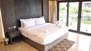 Een moderne hotelkamer met een groot bed, een nachtkastje, een prullenbak en uitzicht op groen via een glazen schuifdeur.