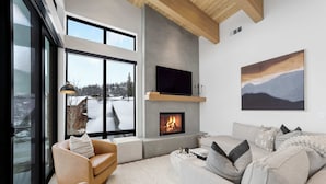 A modern living room with a fireplace, large windows, and a view of a snowy landscape. - OutWest Idaho Ski Condo (Sandpoint)