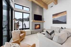 Ein modernes Wohnzimmer mit Kamin, großen Fenstern und Blick auf eine verschneite Landschaft.