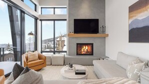 A modern living room with a fireplace, large windows, and a cozy seating area. - OutWest Idaho Ski Condo (Sandpoint)