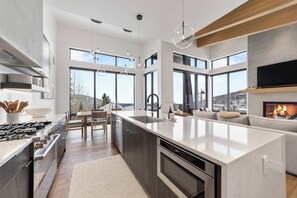 Une cuisine moderne dotée d’un grand îlot central, d’appareils électroménagers intégrés et de grandes fenêtres offrant une vue sur l’extérieur.