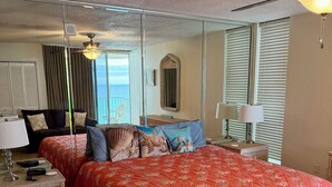 A bedroom with a large bed, a nightstand, a dresser, a mirror, and a view of the ocean through the window.