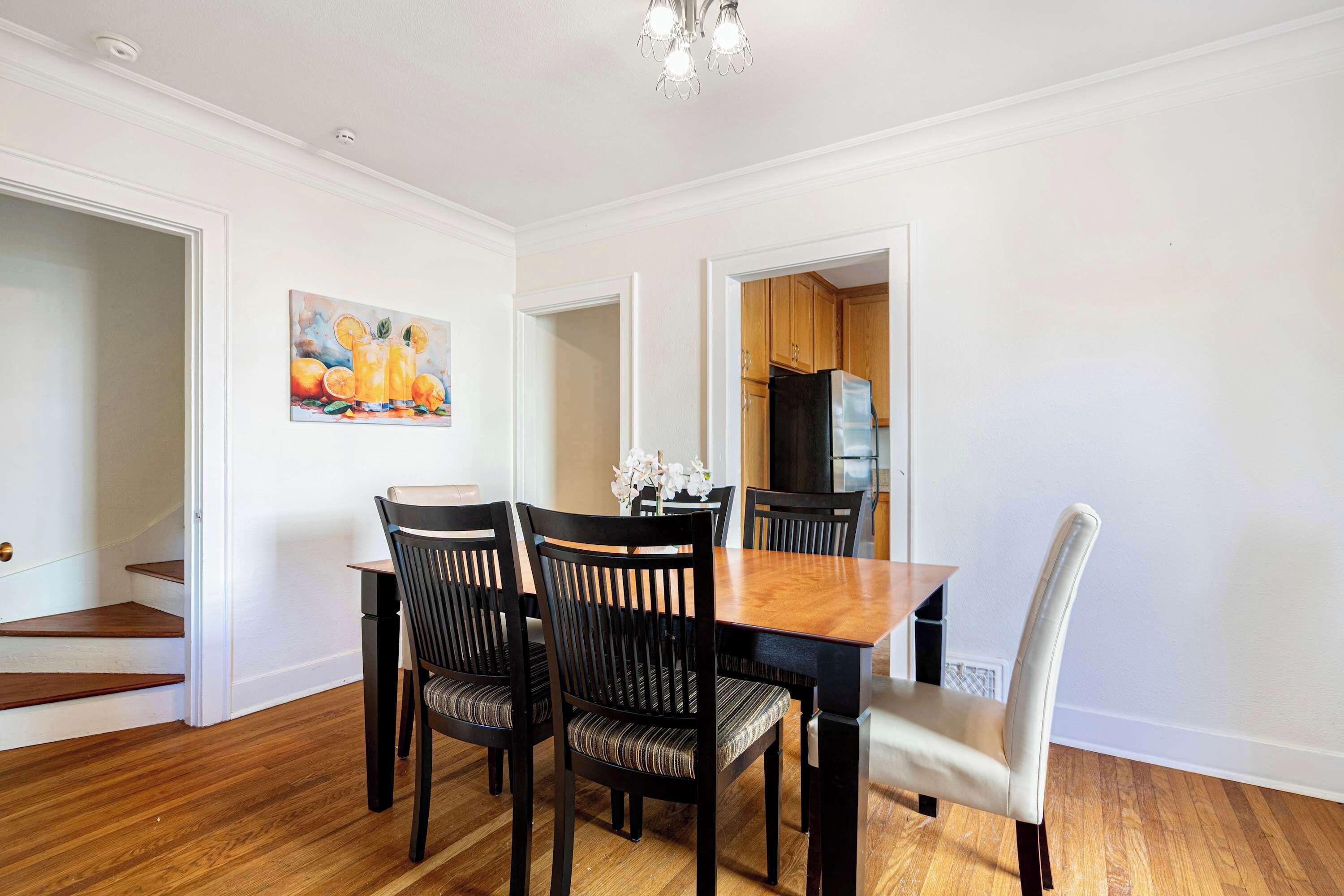 Un coin repas avec une table et des chaises en bois, un tableau au mur et une cuisine en arrière-plan.