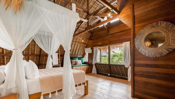 A bedroom with a wooden ceiling, a bed with white bedding, a canopy, and a large mirror on the wall. - Tigerlillys Boutique Hotel (Lembongan Island)