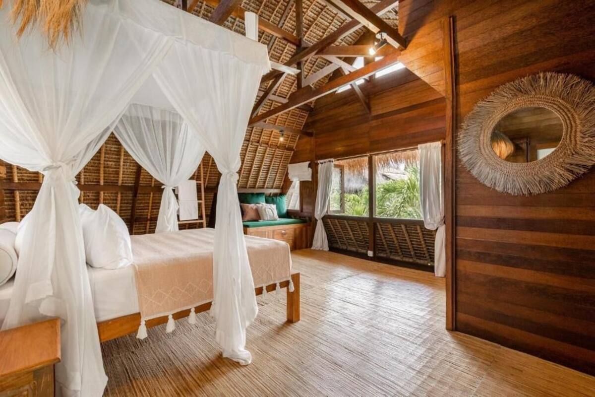 Un dormitorio con techo de madera, una cama con ropa de cama blanca, dosel y un espejo grande en la pared.