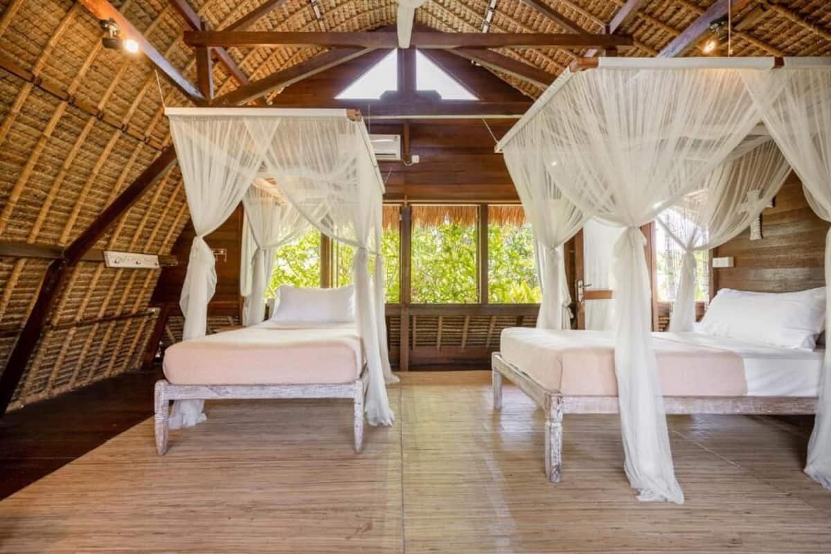 Una habitación con dos camas, cada una con dosel, piso de madera y techo de paja.