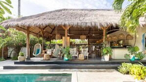 A thatched-roof outdoor seating area with lounge chairs and potted plants. - Tigerlillys Boutique Hotel (Lembongan Island)