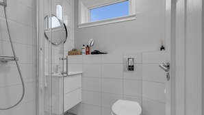 A modern bathroom with a glass shower enclosure, a white toilet, a vanity with a mirror, and a window above the sink.
