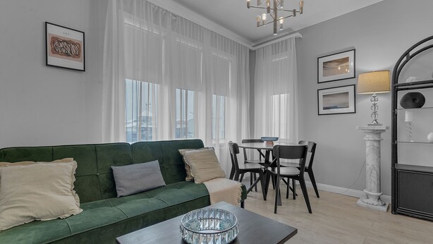 A modern living room with a green sofa, a coffee table, and a dining area with a table and chairs.