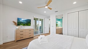 Un dormitorio con una cama grande, un aparador de madera, un ventilador de techo y vistas al exterior.