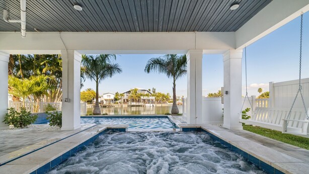 Un área de spa con un jacuzzi, un columpio de madera y vistas a una piscina y palmeras.