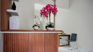A reception desk with a wooden finish, two potted orchids, a framed document, and a chair. - OYO 95054 Prima Jaya Homestay Syariah (Tawang)