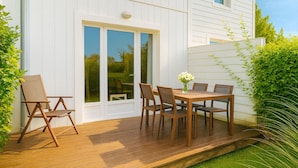 A wooden deck with a table and chairs, a sliding glass door, and a white exterior wall. - Private House in the Normandy Garden – Pierre & Vacances Resort (Branville)