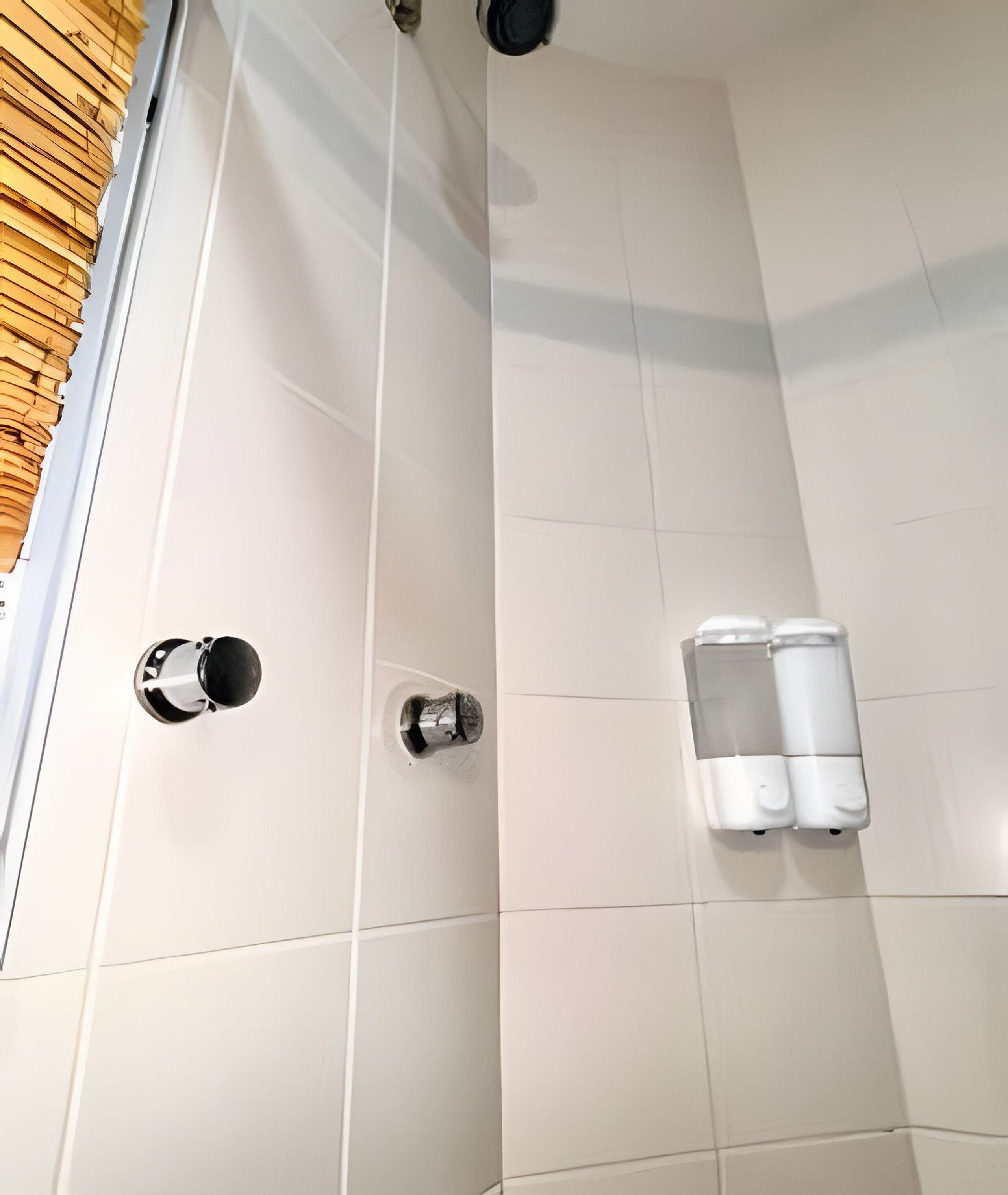 Une salle de bain avec des carreaux blancs, une pomme de douche, un robinet et un distributeur de savon.