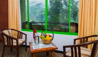 Quarto com duas cadeiras de madeira, uma mesa pequena com uma cesta de frutas e uma janela com moldura verde.