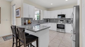 A modern kitchen with white cabinets, granite countertops, stainless steel appliances, and a central island with seating.