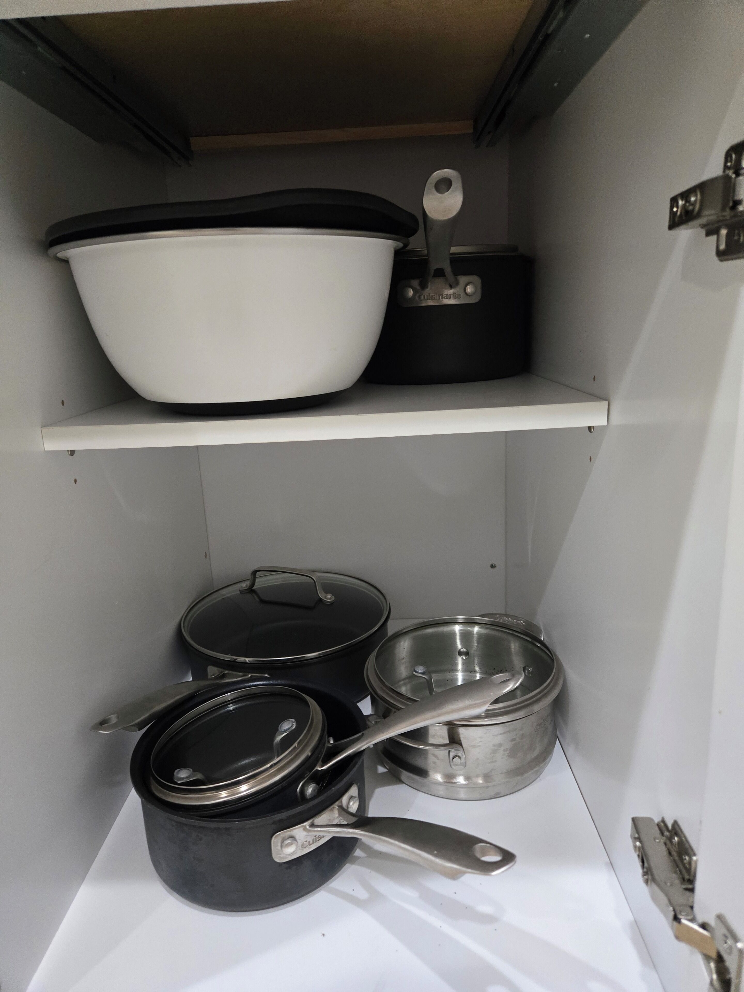 A kitchen cabinet with shelves holding cookware, including pots and pans.