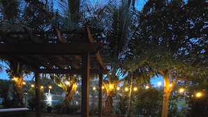 An outdoor patio area with a pergola structure, palm trees, and string lights.