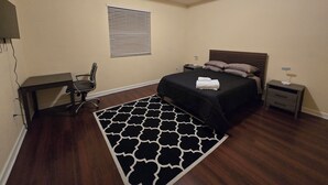 A bedroom with a bed, a desk, a chair, a window with blinds, and a ceiling light.