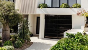 Un edificio moderno de varios pisos con techo plano, ventanas amplias y un jardín cuidado con diferentes plantas y un sendero.