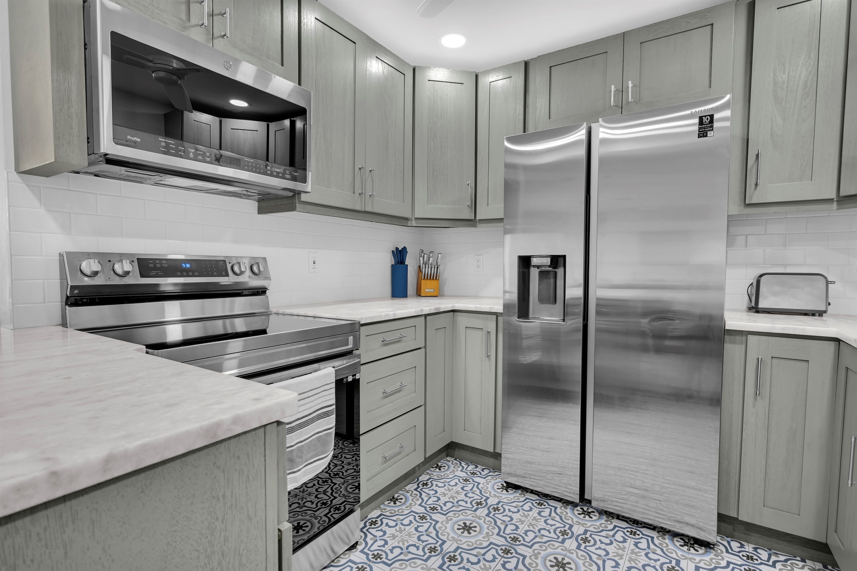Una cocina moderna con electrodomésticos de acero inoxidable, armarios de madera clara y baldosas de suelo con diseño.