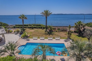 Ein Pool mit Blick auf das Meer, umgeben von Palmen und Liegestühlen.