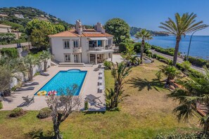 Ein zweistöckiges Haus mit Swimmingpool, umgeben von Palmen und Blick auf das Meer.