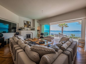Ein modernes Wohnzimmer mit Kamin, einer Sofagarnitur, einem Couchtisch und Meerblick.