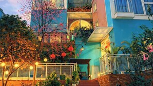 A multi-story building with a staircase leading to the entrance, surrounded by potted plants and a scooter parked outside. - Rose Hill Villa Dalat (Cam Ly - Da Lat)
