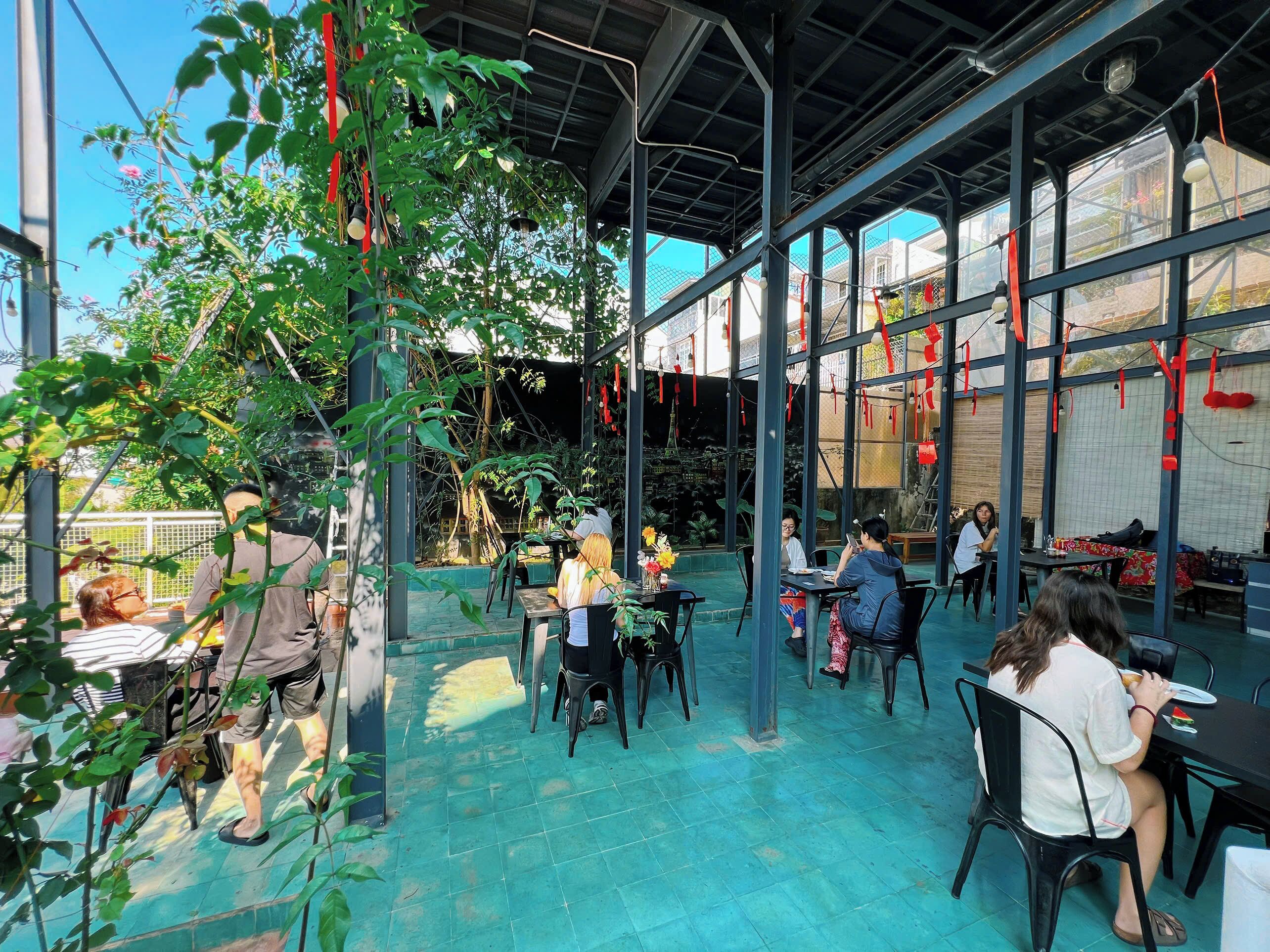 Ein Terrassenbereich im Freien mit Tischen und Stühlen, umgeben von Pflanzen und roten Dekorationen.