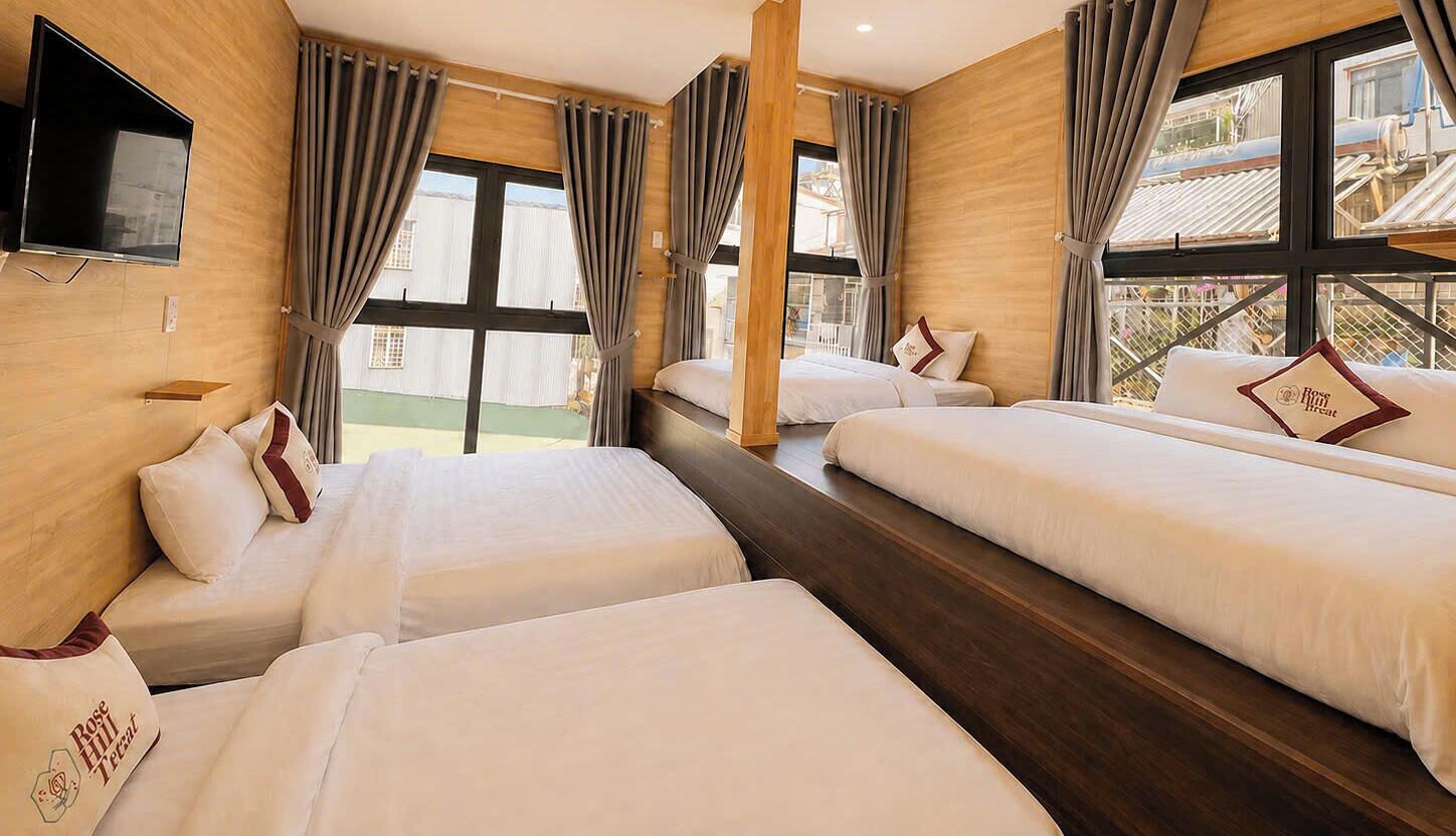 A hotel room with three beds, a TV, and large windows with curtains.