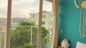 A bedroom with a large window, a view of the city, a bed, a small plant, and a decorative item on the nightstand. - Rose Hill Villa Dalat (Cam Ly - Da Lat)