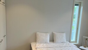 Ein Schlafzimmer mit einem Bett, weißen Wänden, einem Fenster und einem Holzboden.