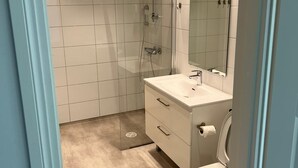 Ein modernes Badezimmer mit begehbarer Dusche, Toilette und Waschtisch mit Spiegel.