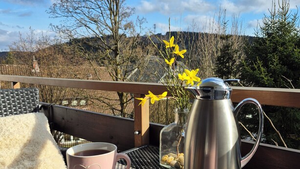 En morgenmadsopsætning med croissanter, kaffekopper og en termokande på et metalbord udendørs.