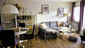 En moderne stue med en grå sofa, et spisebord med stole og et hvidt bogreol.