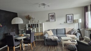En moderne stue med en grå sofa, et spisebord med stole, et hvidt skab og en loftlampe.