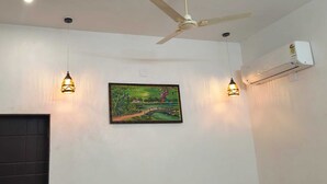 A room with a ceiling fan, two wall-mounted lights, an air conditioning unit, and a framed painting. - Pearl Pride Villa (Udaipur)