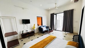 A hotel room with a bed, a desk, a TV, and a window with curtains. - Pearl Pride Villa (Udaipur)