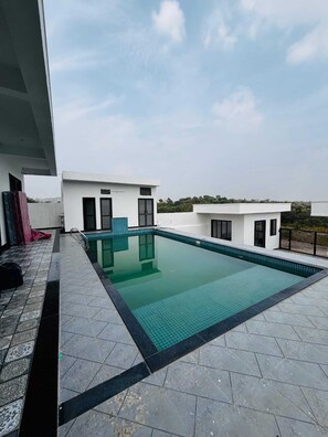 A rooftop swimming pool with a clear blue water surface, surrounded by a tiled deck and a white building with black-framed windows. - Pearl Pride Villa (Udaipur)