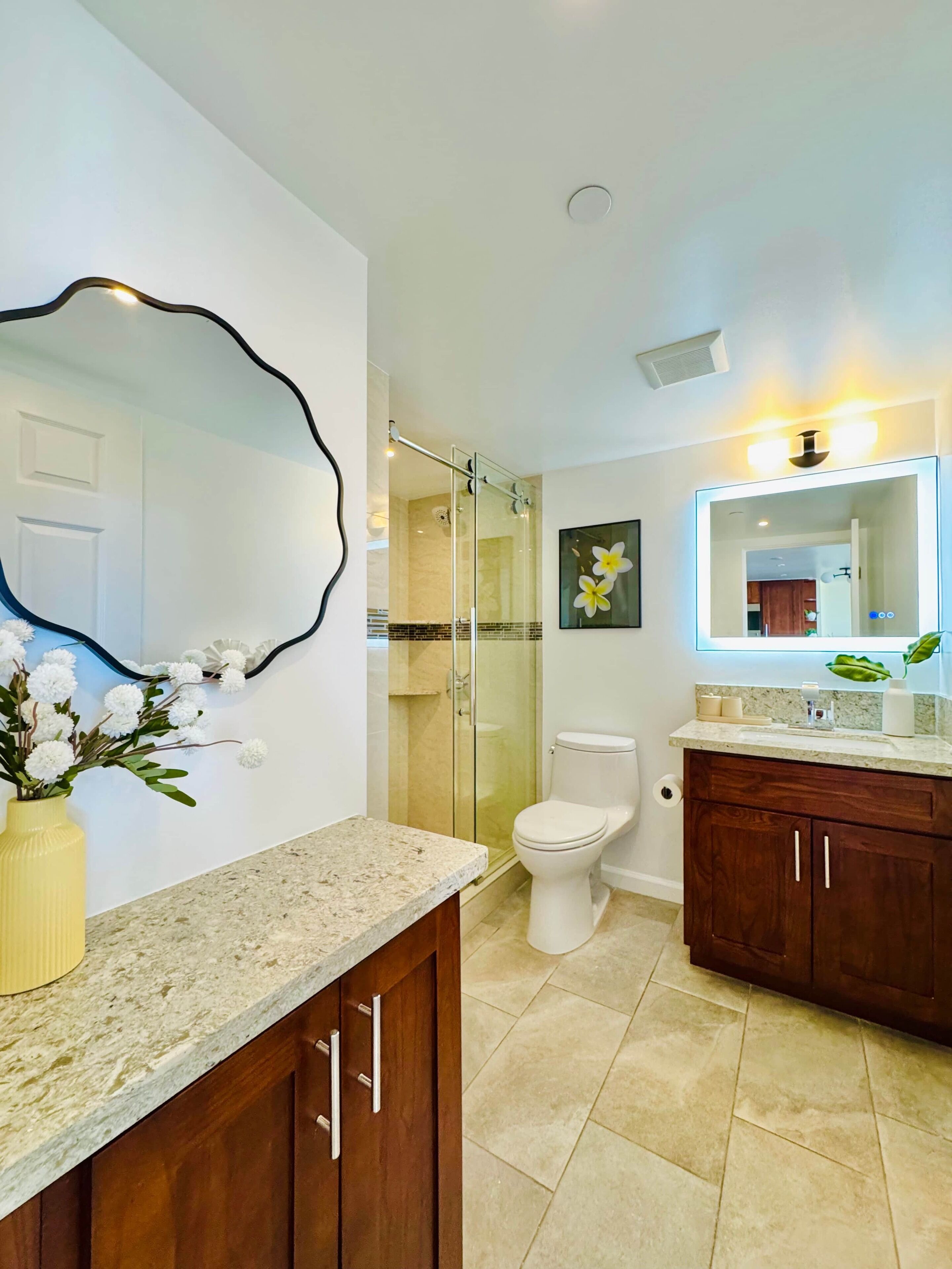 A modern bathroom with a glass shower enclosure, a toilet, a vanity with a sink, and a large mirror.