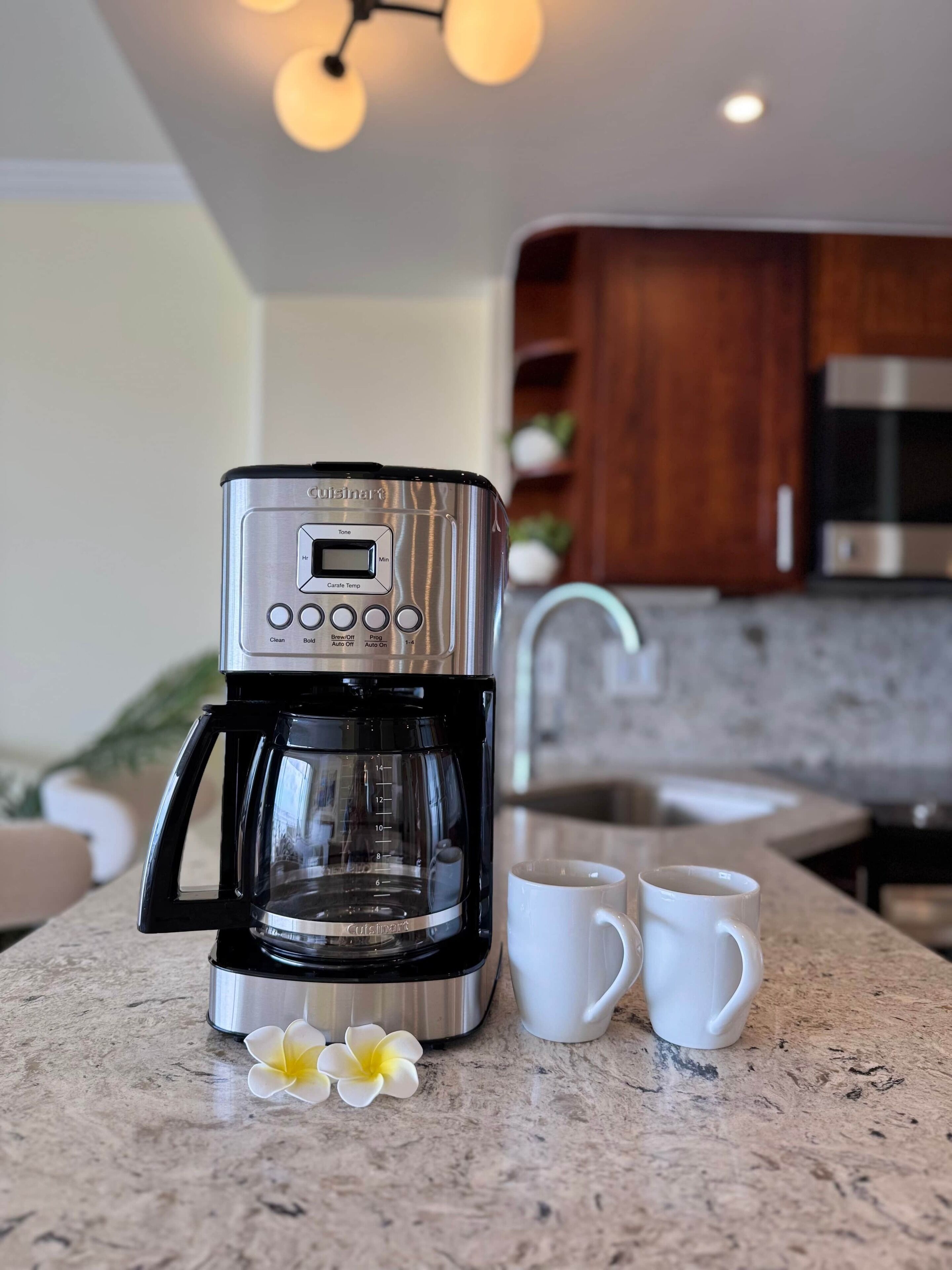 Une machine à café est posée sur un plan de travail de cuisine, avec deux tasses blanches à côté.