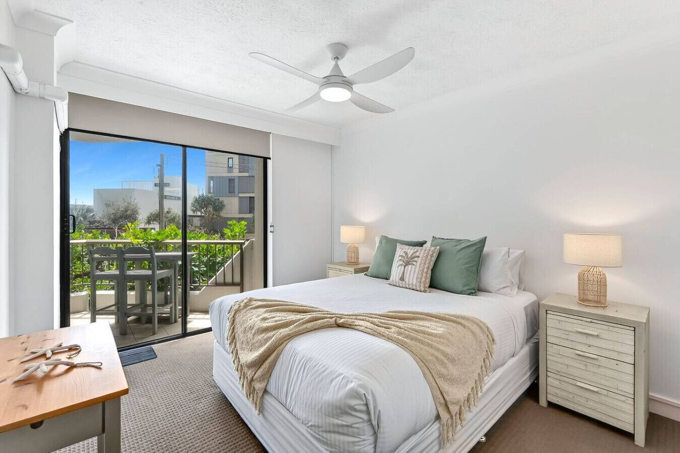 A bedroom with a bed, bedside tables, a ceiling fan, and a sliding glass door to a balcony.