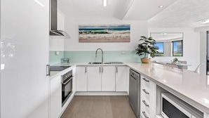 Una cocina moderna con armarios blancos, un lavamanos de acero inoxidable y un amplio ventanal con vista al océano.