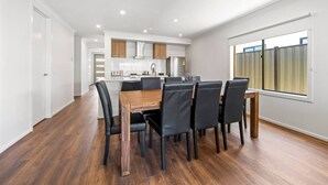 A modern kitchen with white cabinets, a wooden dining table, and black chairs. - New Luxury Home • Perfect for Families & WorkStays (Mickleham)