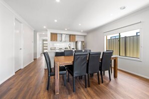 A modern kitchen with white cabinets, a wooden dining table, and black chairs. - New Luxury Home • Perfect for Families & WorkStays (Mickleham)