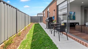 A modern outdoor patio with a barbecue grill, seating area, and a well-maintained lawn. - New Luxury Home • Perfect for Families & WorkStays (Mickleham)