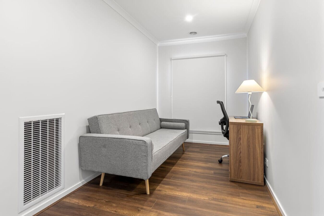 Ein kleiner, moderner Raum mit einem grauen Sofa, einem Holztisch mit einer Lampe und einer weißen Tür.